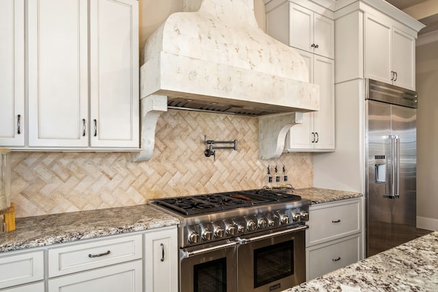 kitchen featuring premium range hood, premium appliances, tasteful backsplash, white cabinets, and light stone counters