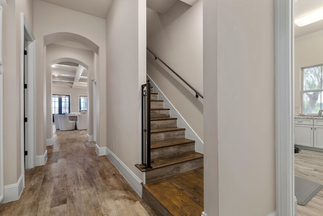 stairway featuring beam ceiling, wood-type flooring, and coffered ceiling