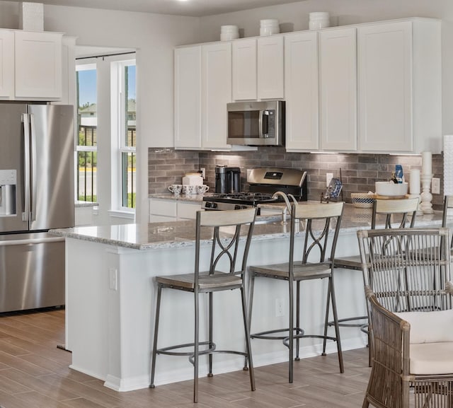 kitchen featuring white cabinetry, light hardwood / wood-style floors, stainless steel appliances, light stone counters, and a breakfast bar