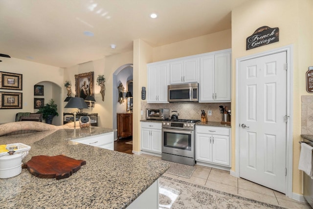 kitchen featuring light tile patterned floors, light stone counters, stainless steel appliances, and white cabinetry