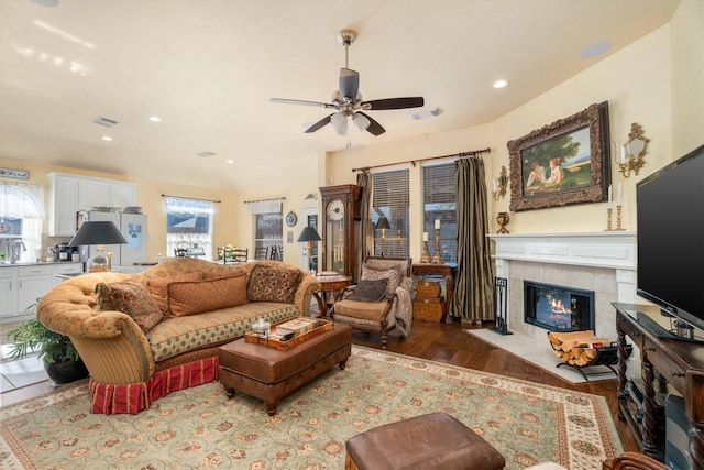 living room featuring ceiling fan, a healthy amount of sunlight, wood-type flooring, and a tile fireplace