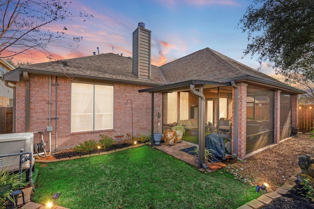 back house at dusk with a yard and a sunroom