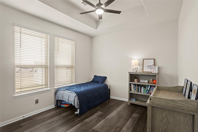 bedroom featuring ceiling fan, dark hardwood / wood-style flooring, a tray ceiling, and multiple windows