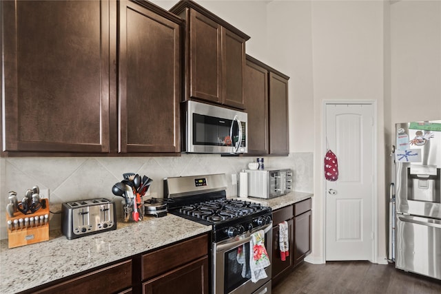 kitchen featuring dark brown cabinetry, appliances with stainless steel finishes, dark wood-type flooring, tasteful backsplash, and light stone counters