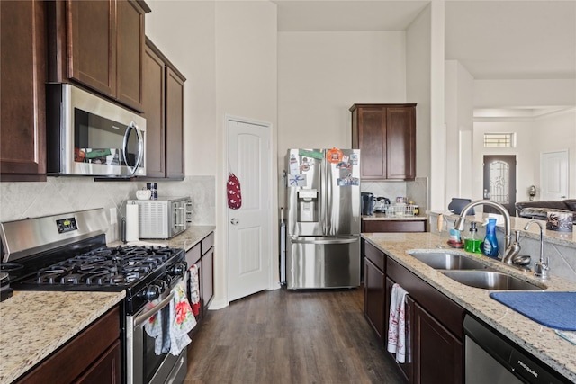 kitchen with light stone countertops, dark brown cabinetry, dark hardwood / wood-style flooring, stainless steel appliances, and sink