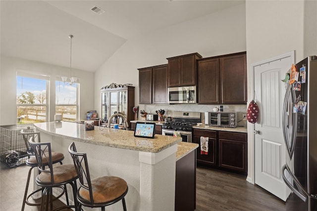 kitchen with appliances with stainless steel finishes, decorative light fixtures, a kitchen bar, dark hardwood / wood-style flooring, and light stone counters