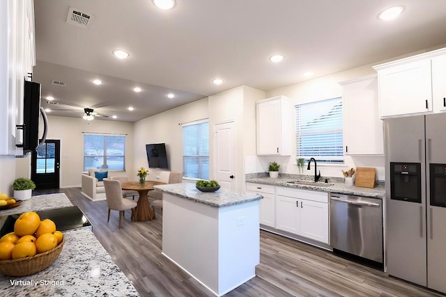 kitchen with dishwasher, a kitchen island, sink, light stone countertops, and white cabinets