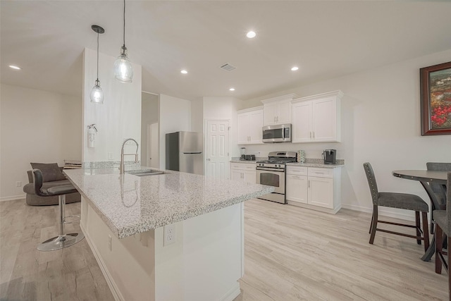 kitchen featuring pendant lighting, a kitchen bar, light stone countertops, appliances with stainless steel finishes, and white cabinets