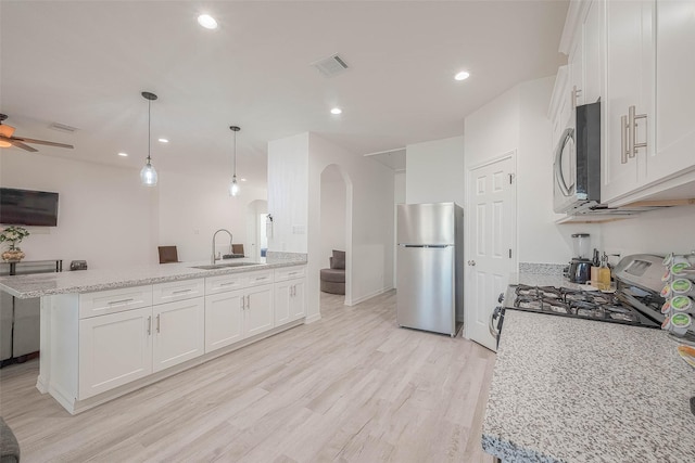 kitchen with ceiling fan, stainless steel appliances, white cabinets, light stone counters, and sink