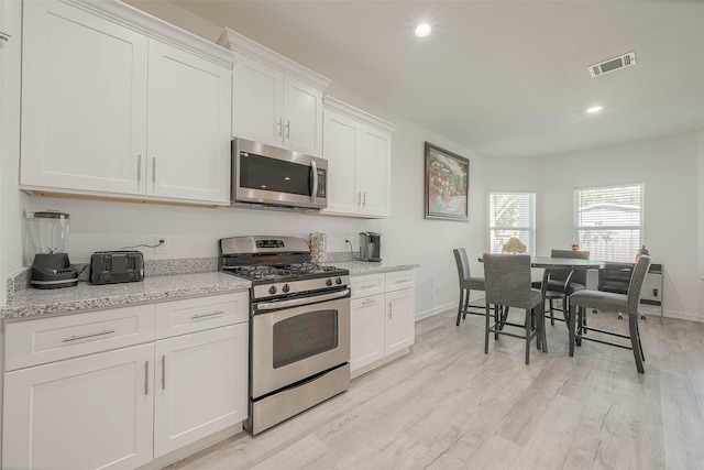 kitchen featuring light stone countertops, white cabinetry, light hardwood / wood-style flooring, and stainless steel appliances