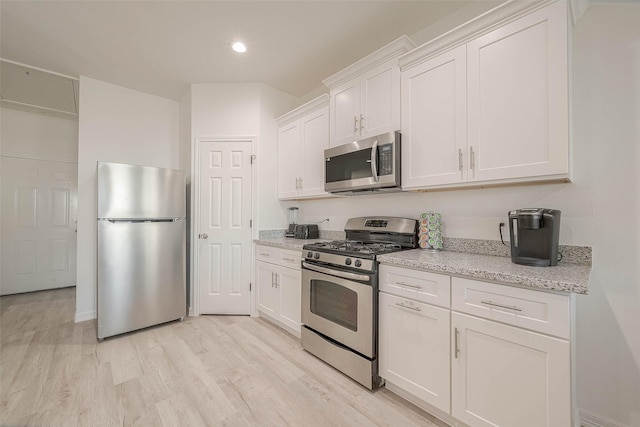 kitchen featuring light stone countertops, white cabinets, appliances with stainless steel finishes, and light hardwood / wood-style flooring