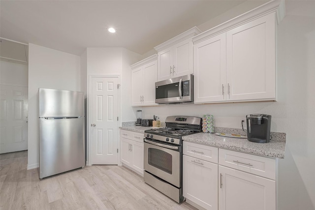 kitchen with light stone counters, white cabinets, stainless steel appliances, and light wood-type flooring