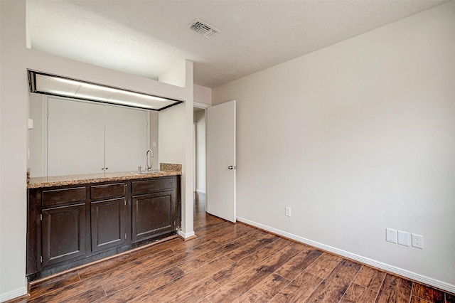 unfurnished bedroom with a sink, visible vents, baseboards, and dark wood finished floors