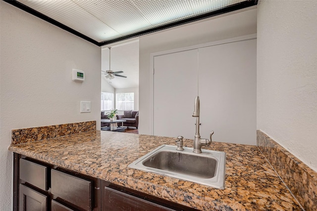 kitchen featuring a ceiling fan, a sink, vaulted ceiling, dark brown cabinets, and a textured wall