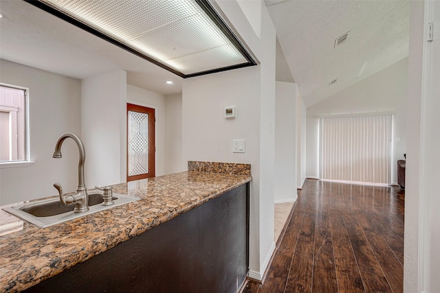 kitchen with hardwood / wood-style floors, light stone counters, baseboards, visible vents, and a sink