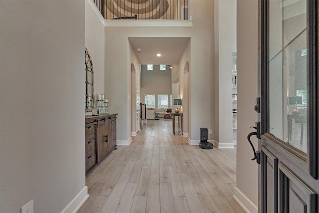 foyer entrance featuring light wood-type flooring, baseboards, a high ceiling, and arched walkways