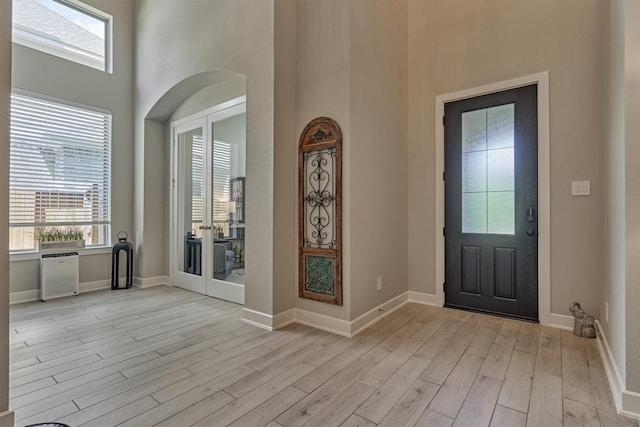 entryway featuring a towering ceiling, light wood-style floors, baseboards, and french doors