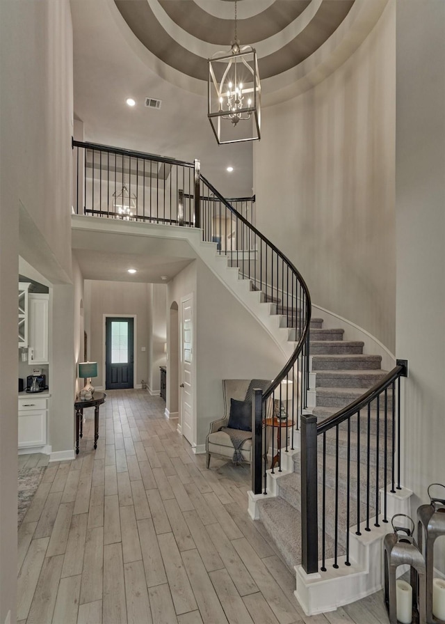 foyer featuring light wood-type flooring, a towering ceiling, and a raised ceiling