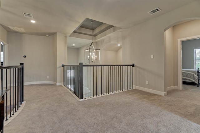 corridor featuring a tray ceiling, light carpet, and an inviting chandelier