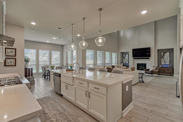 kitchen with pendant lighting, white cabinetry, a fireplace, a kitchen island with sink, and stainless steel dishwasher