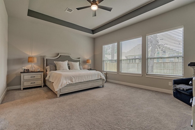 bedroom with a tray ceiling, light colored carpet, visible vents, a ceiling fan, and baseboards