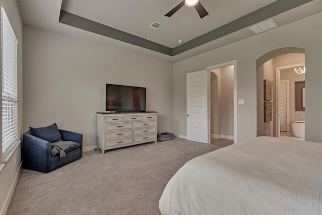 bedroom with ceiling fan, ensuite bath, a tray ceiling, and light colored carpet