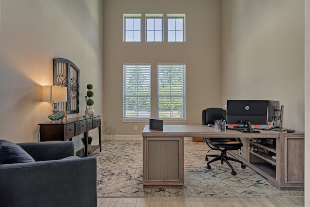 office space featuring a towering ceiling and light wood-type flooring