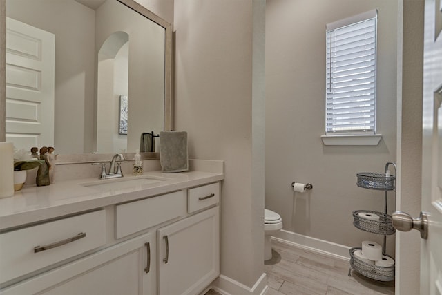 half bathroom with baseboards, vanity, toilet, and wood finished floors