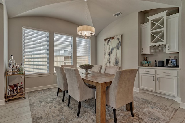 dining room featuring light wood-style floors, visible vents, vaulted ceiling, and baseboards