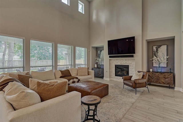 living room featuring a towering ceiling, plenty of natural light, light hardwood / wood-style flooring, and a stone fireplace