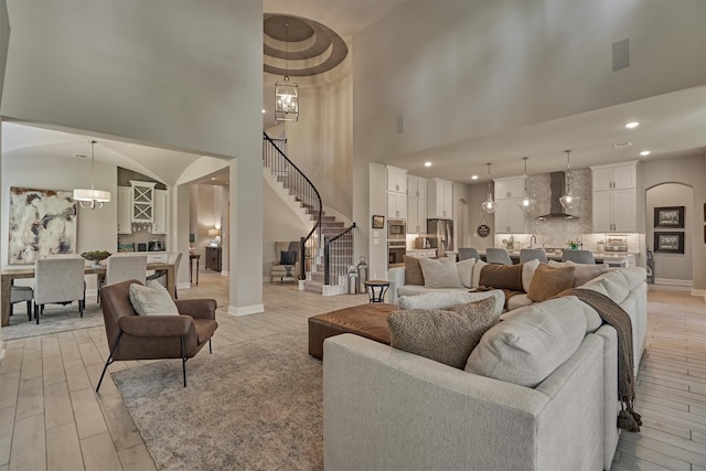 living room featuring light wood-style floors, stairs, arched walkways, and an inviting chandelier