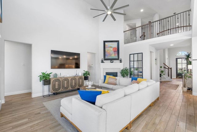 living room featuring ceiling fan, a high ceiling, and light hardwood / wood-style flooring