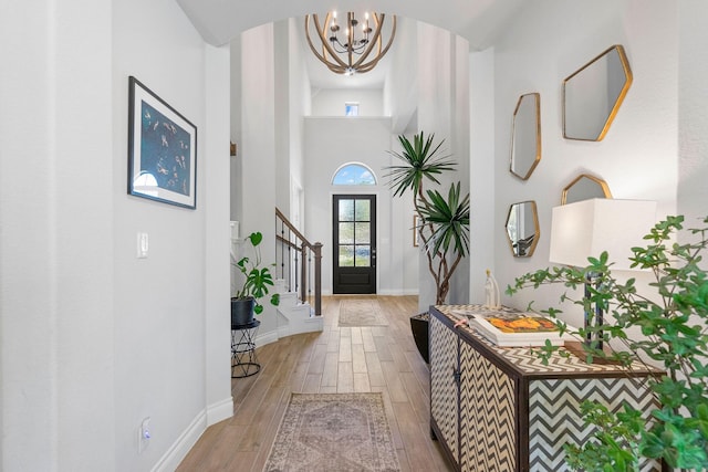 foyer entrance featuring a towering ceiling, an inviting chandelier, and light hardwood / wood-style floors