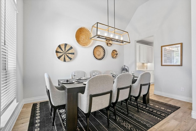 dining space with light wood-type flooring, vaulted ceiling, and a notable chandelier