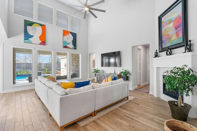 living room with ceiling fan, light hardwood / wood-style floors, and a towering ceiling