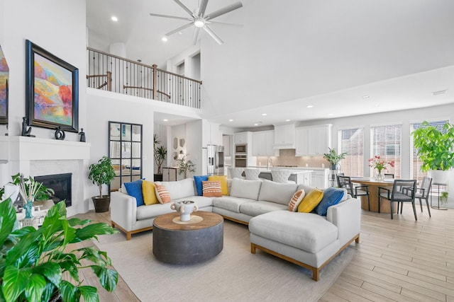 living room with ceiling fan, a high ceiling, sink, and a tiled fireplace