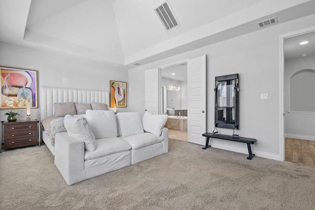 bedroom with high vaulted ceiling, light colored carpet, ensuite bathroom, and a raised ceiling