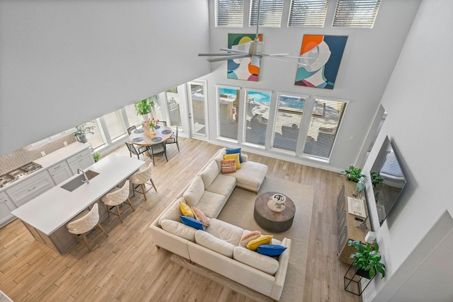 living room featuring ceiling fan, light hardwood / wood-style floors, a high ceiling, and sink