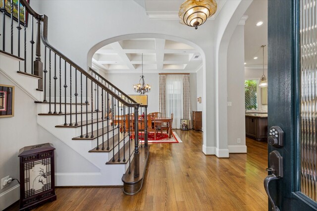 entrance foyer with beam ceiling, wood-type flooring, an inviting chandelier, coffered ceiling, and ornamental molding