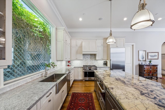 kitchen featuring light stone counters, a sink, wall chimney range hood, ornamental molding, and high end appliances