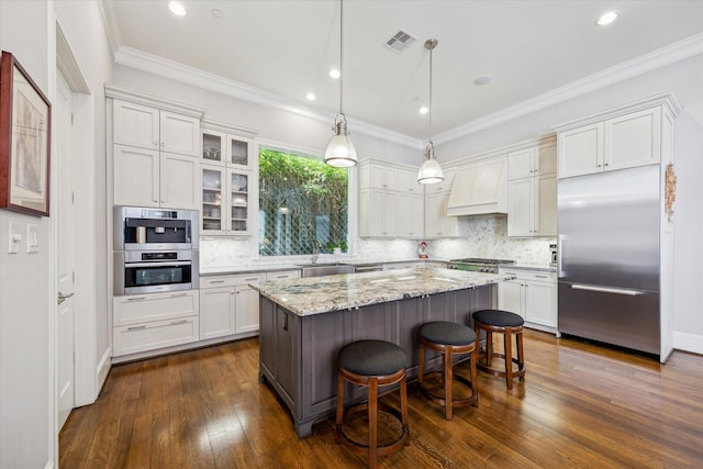 kitchen with visible vents, custom range hood, appliances with stainless steel finishes, a breakfast bar area, and a center island