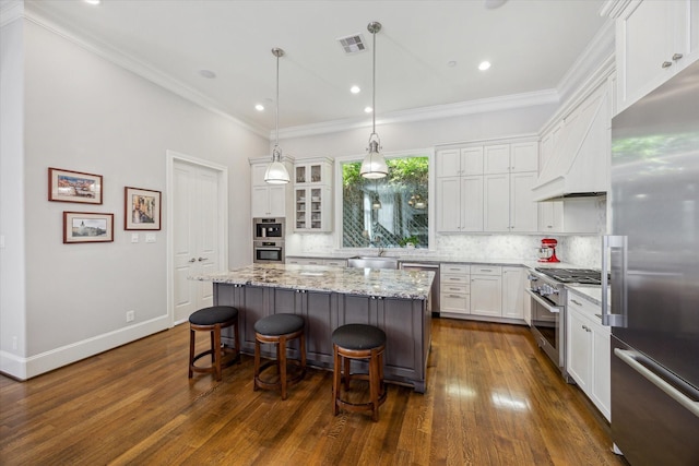 kitchen featuring premium appliances, a breakfast bar, visible vents, white cabinets, and a center island