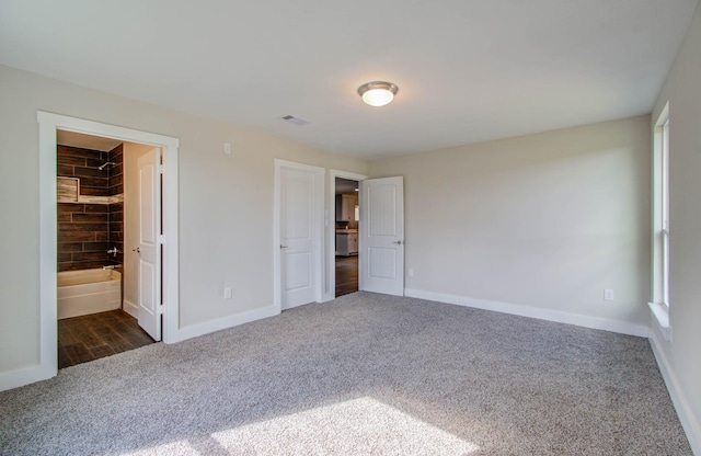 unfurnished bedroom with ensuite bath, a closet, a walk in closet, and dark colored carpet