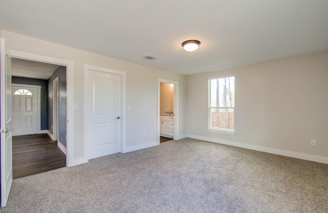 unfurnished bedroom with connected bathroom and dark colored carpet