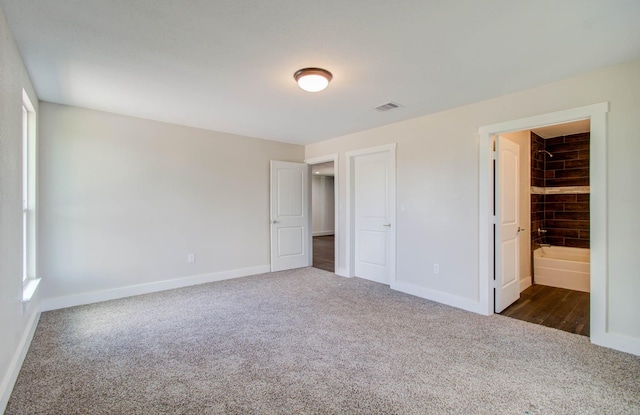 unfurnished bedroom featuring multiple windows, dark carpet, ensuite bathroom, and a closet