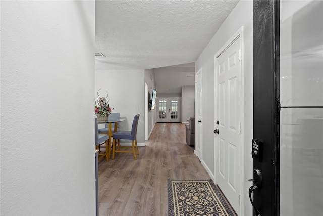 corridor featuring a textured ceiling, light hardwood / wood-style floors, and french doors