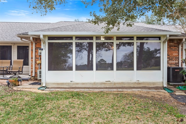 rear view of property featuring brick siding, central AC unit, a shingled roof, and a sunroom