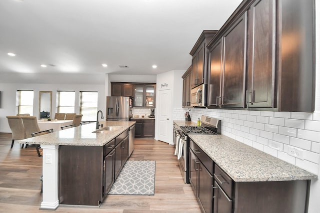 kitchen with a sink, decorative backsplash, stainless steel appliances, light wood-type flooring, and dark brown cabinets