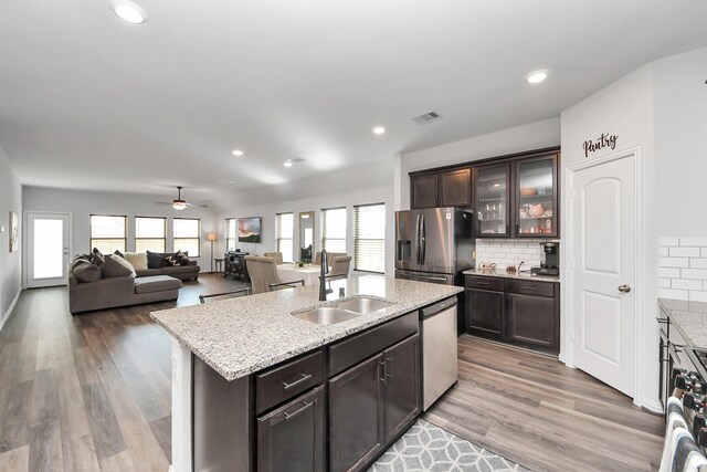 kitchen with a sink, a center island with sink, dark brown cabinetry, visible vents, and appliances with stainless steel finishes