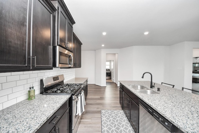 kitchen featuring light stone counters, a sink, stainless steel appliances, wood finished floors, and backsplash